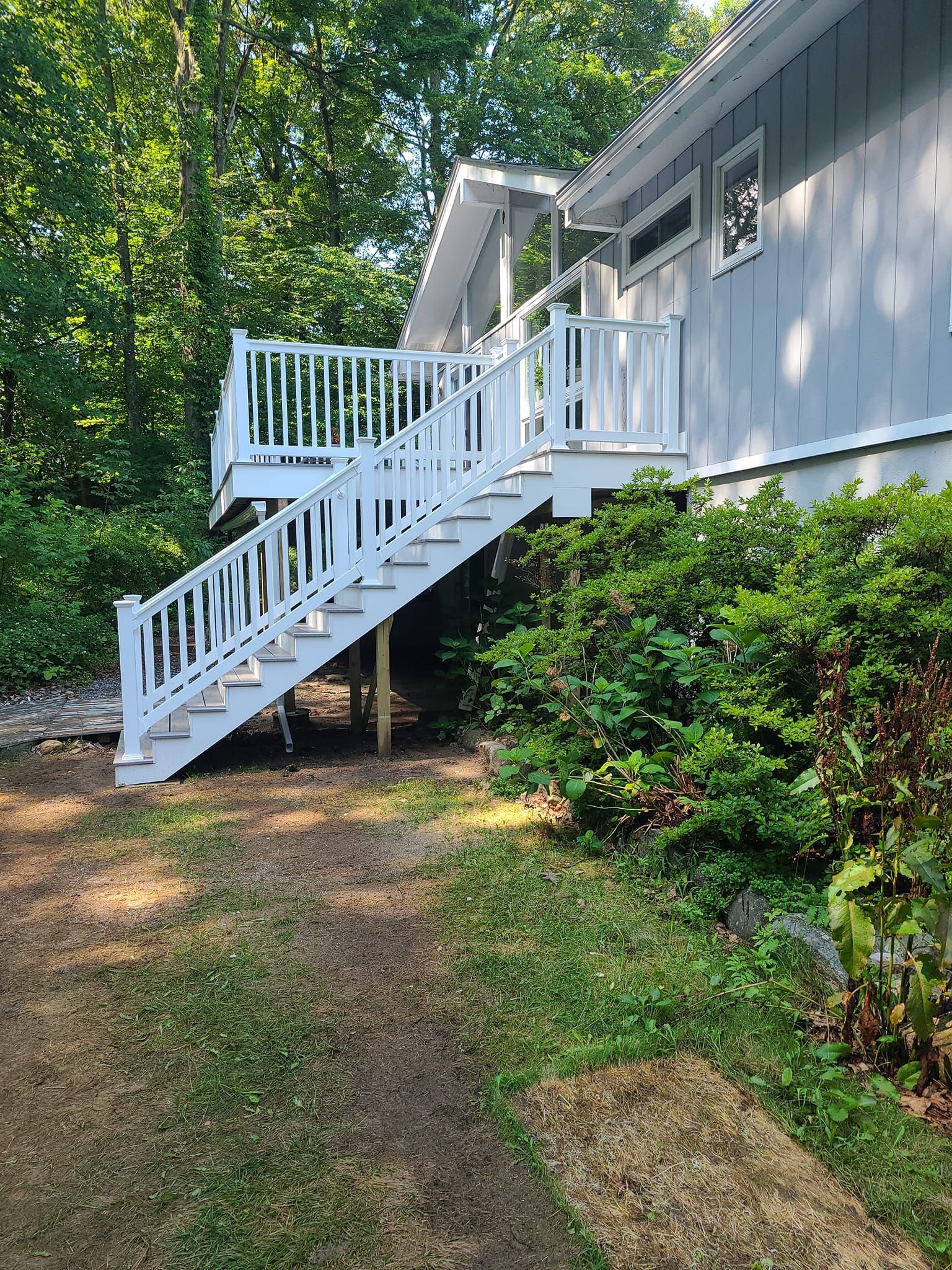 A white deck with stairs leading up to it is in front of a house.