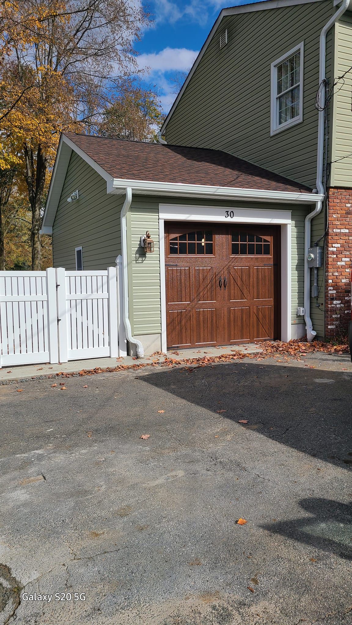 A green house with a brown garage door and a white fence.
