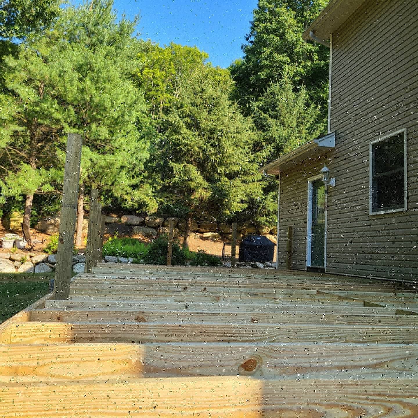 A wooden deck is being built in front of a house surrounded by trees.