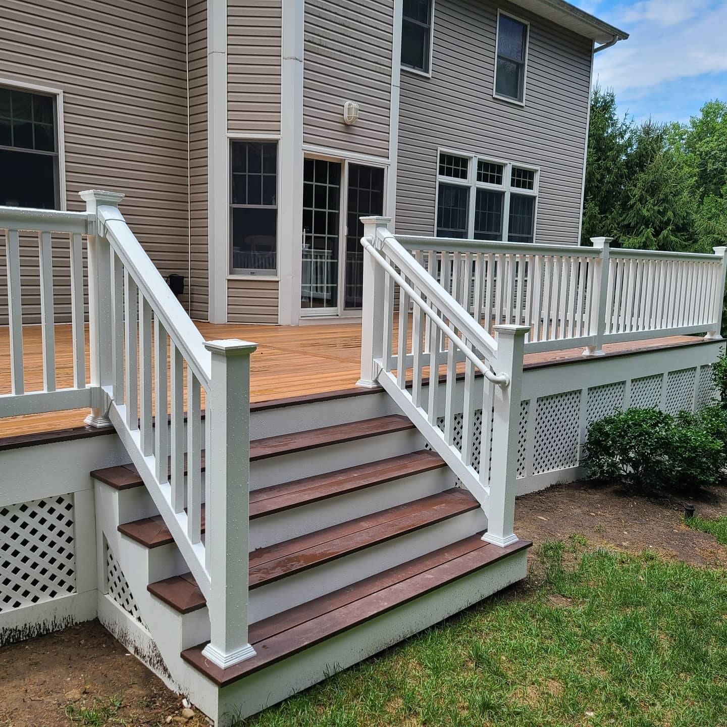 A deck with stairs and a white railing in front of a house