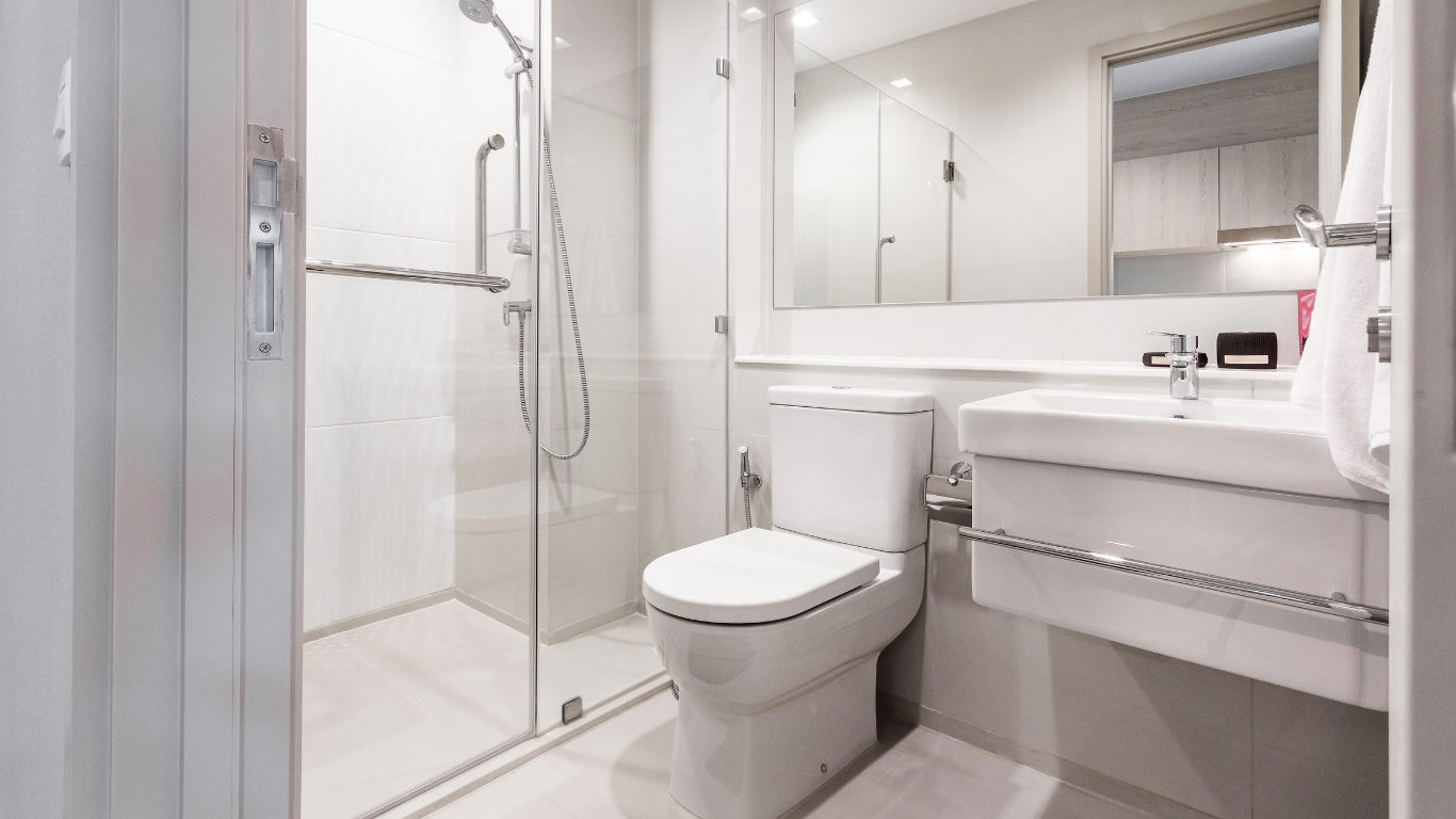A clean, modern bathroom with a toilet, sink, and a walk-in shower with glass doors. Mostly white with chrome fixtures.