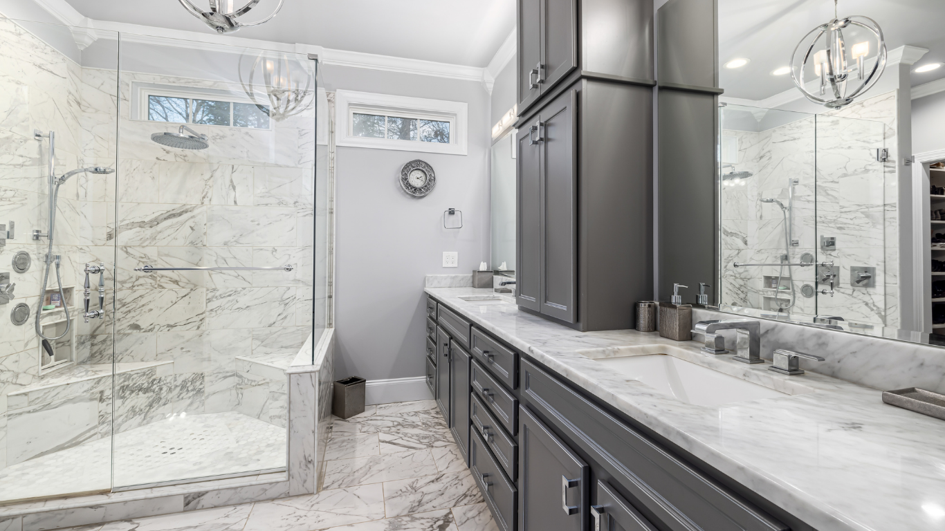Spacious, luxurious bathroom featuring a marble shower and countertop, gray cabinets, and large mirror.
