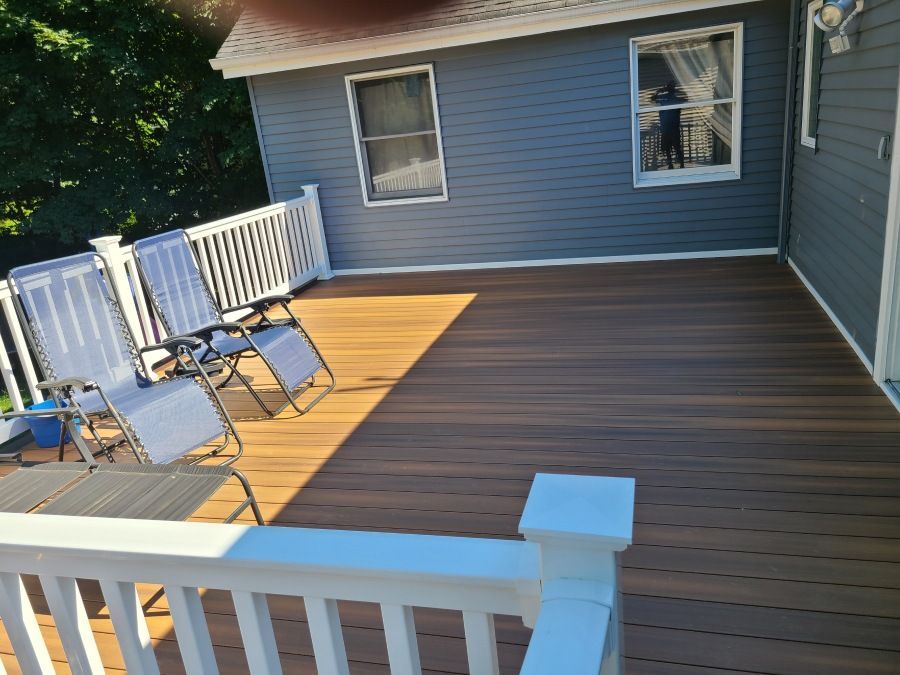 A wooden deck with chairs and a white railing in front of a blue house.