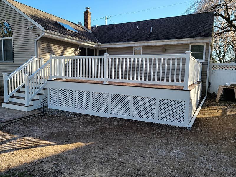 A white deck with stairs is in the backyard of a house.