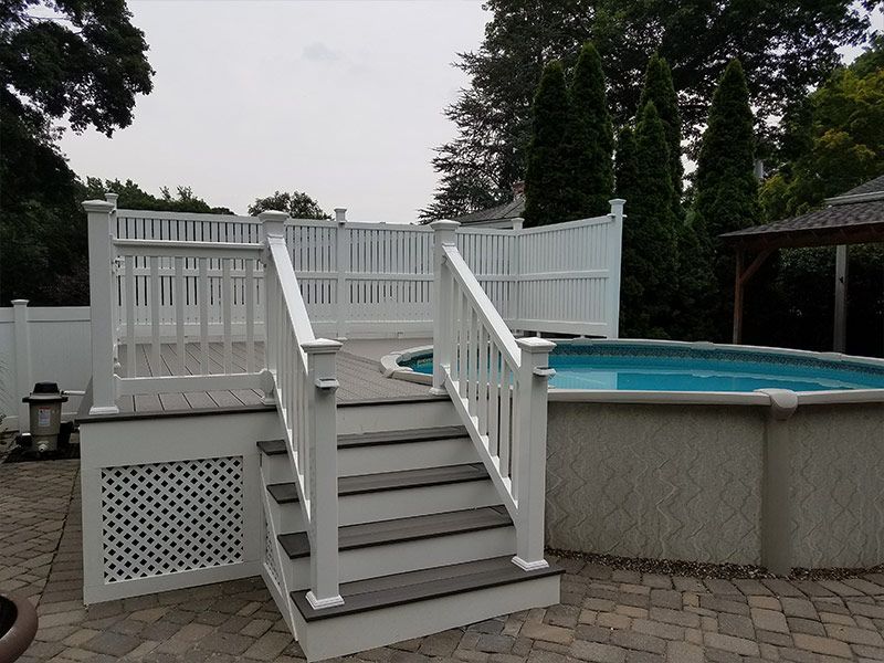 A white deck with stairs leading up to a pool