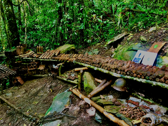 Kokoda Track hikers with backpacks wade through a shallow, rocky stream in a lush green Papua New Guinea jungle.