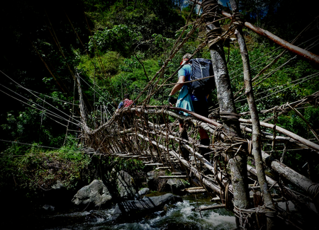 Kokoda Track hikers with backpacks wade through a shallow, rocky stream in a lush green Papua New Guinea jungle.