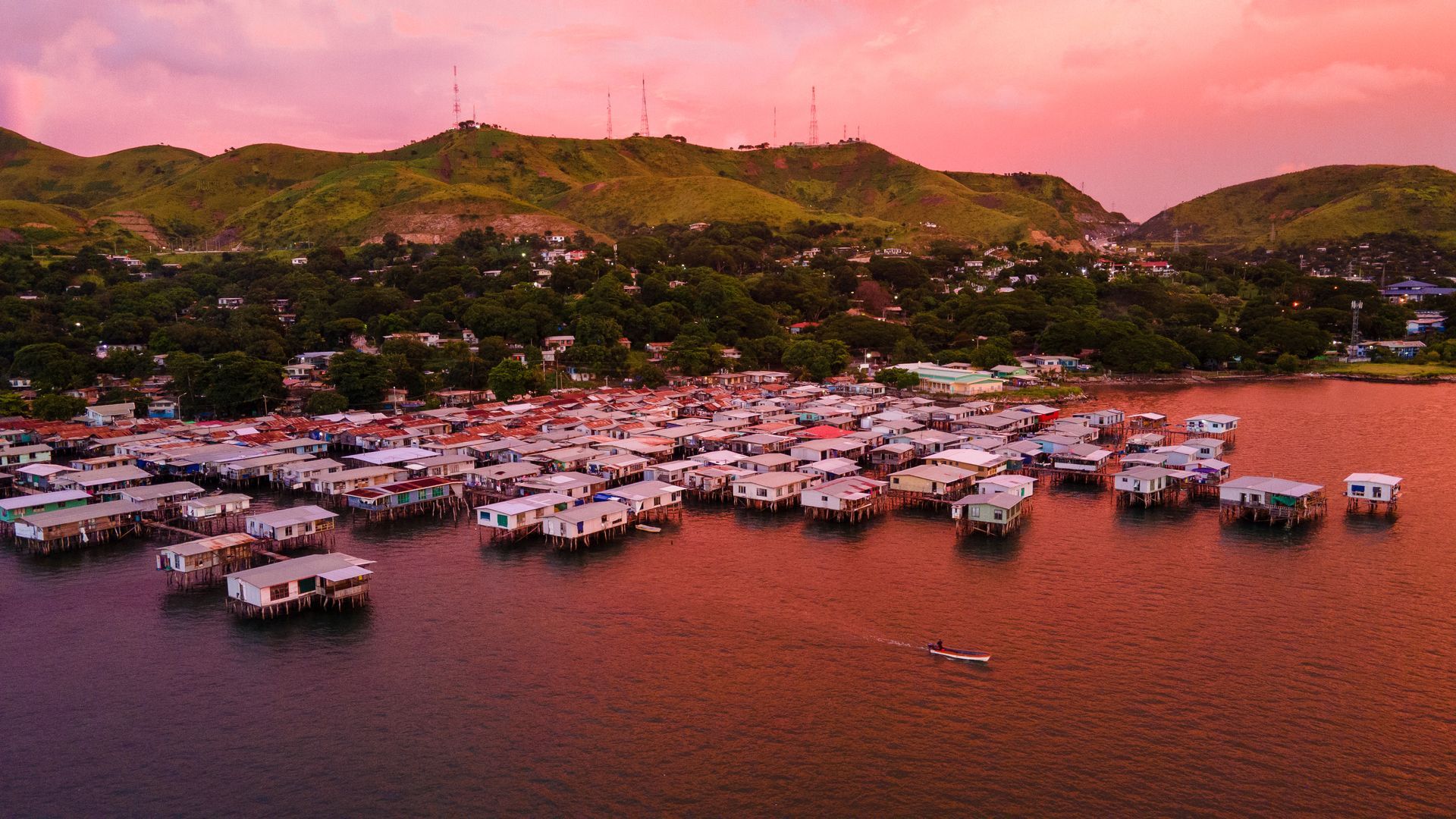 Image depicts a village on water in the city of Port Moresby. Wooden homes built on stilts, hovering over the water accessible by treacherous board walks.