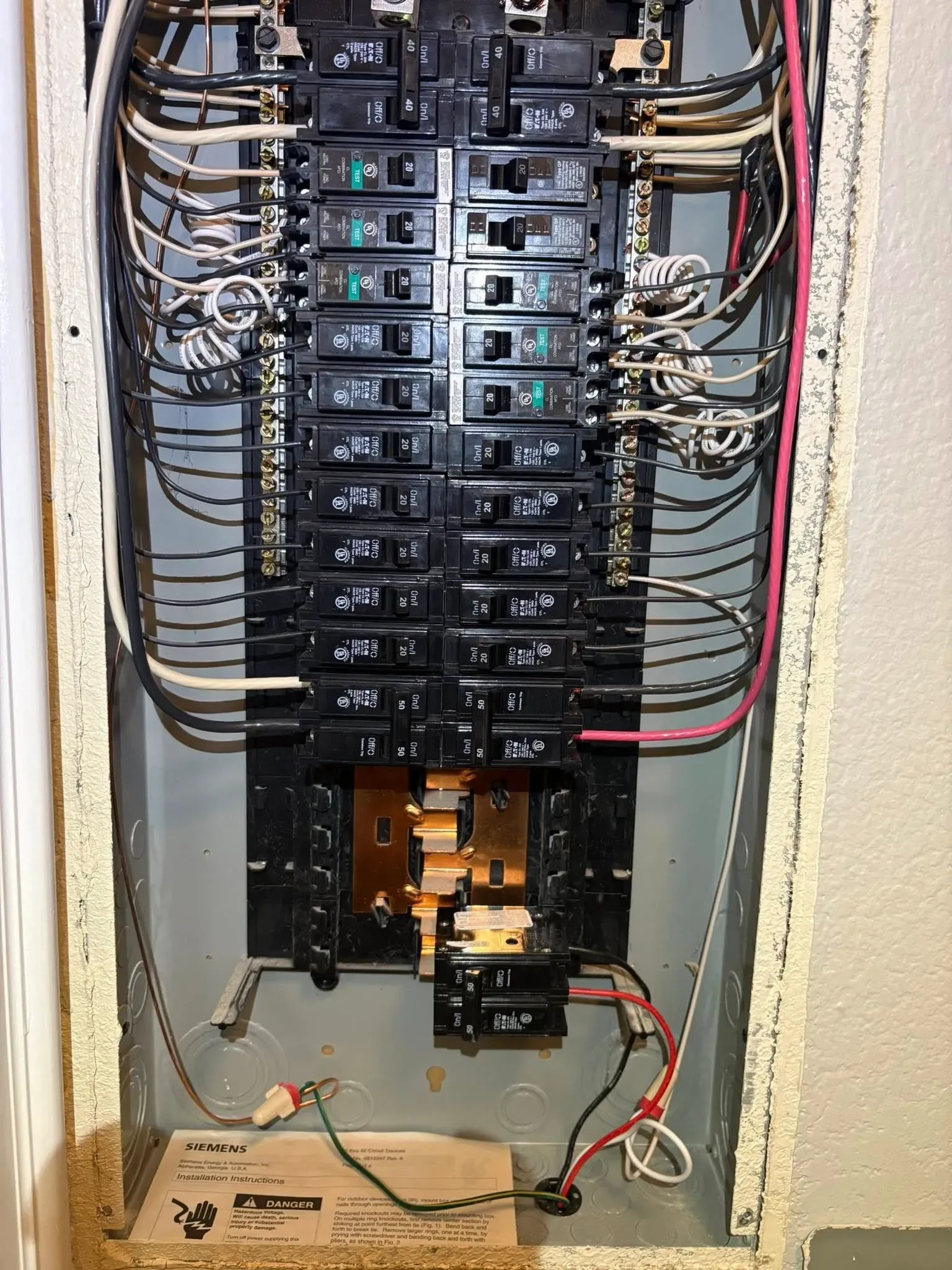 Open electrical breaker panel with multiple circuit breakers and exposed wiring inside a wall recess
