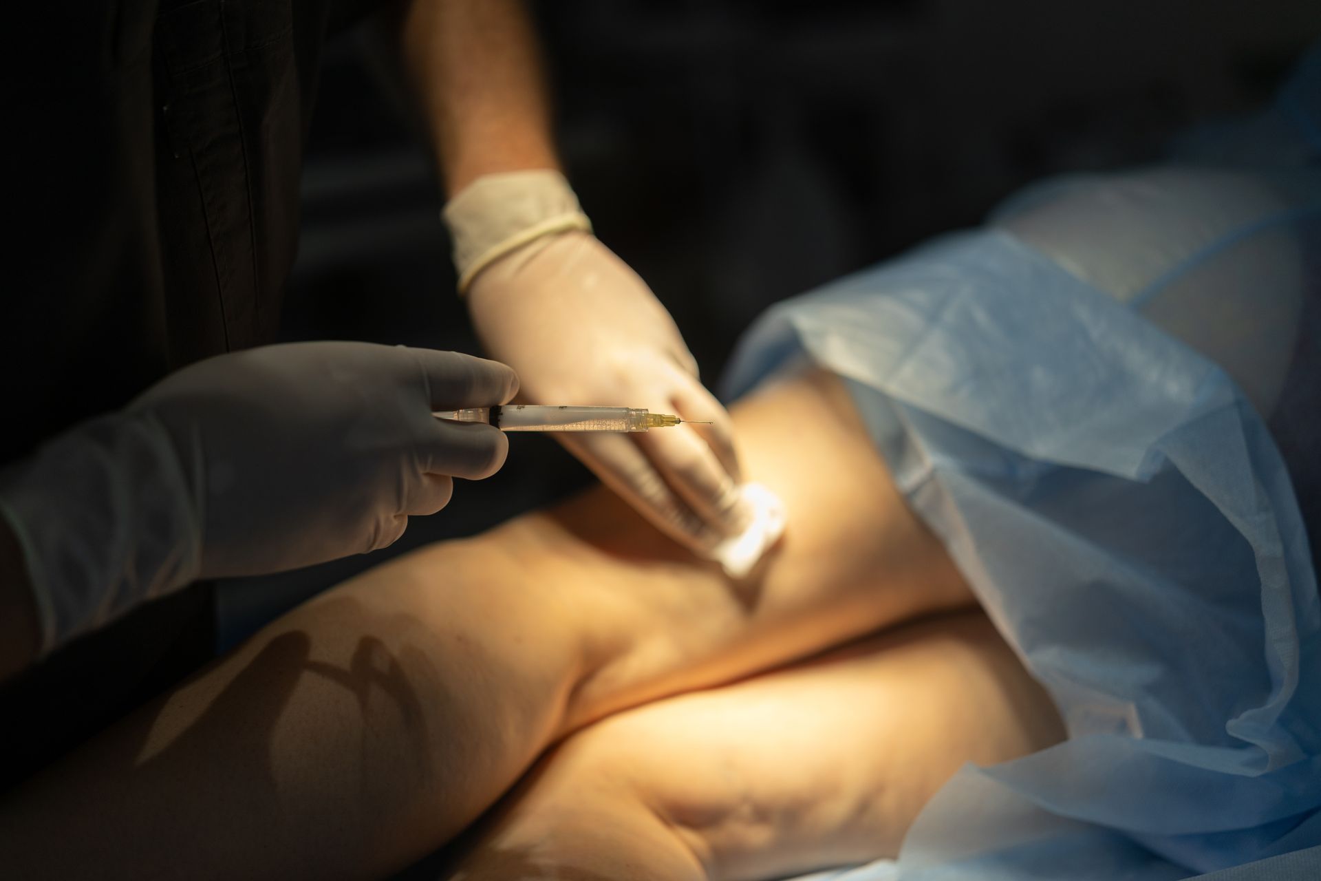 Medical professional administering an injection to a patient’s leg during a procedure.