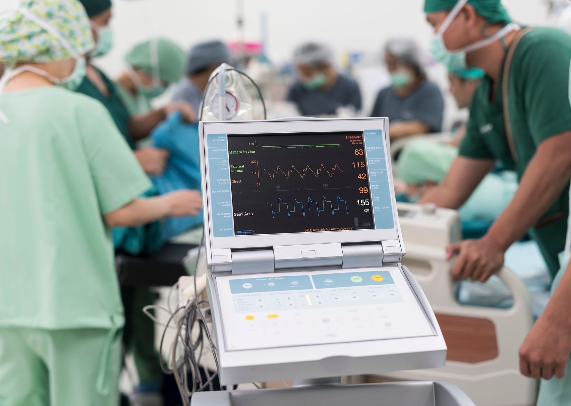 Medical monitor displaying vital signs in an operating room, surrounded by medical staff. Medical monitor displaying vital signs in an operating room, surrounded by medical staff.