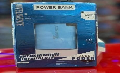 Caja azul para batería externa con ventana transparente y texto en español, mostrada sobre una superficie roja.