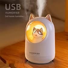 Humidificador USB blanco con orejas de gato que brillan en naranja sobre una mesa de madera.
