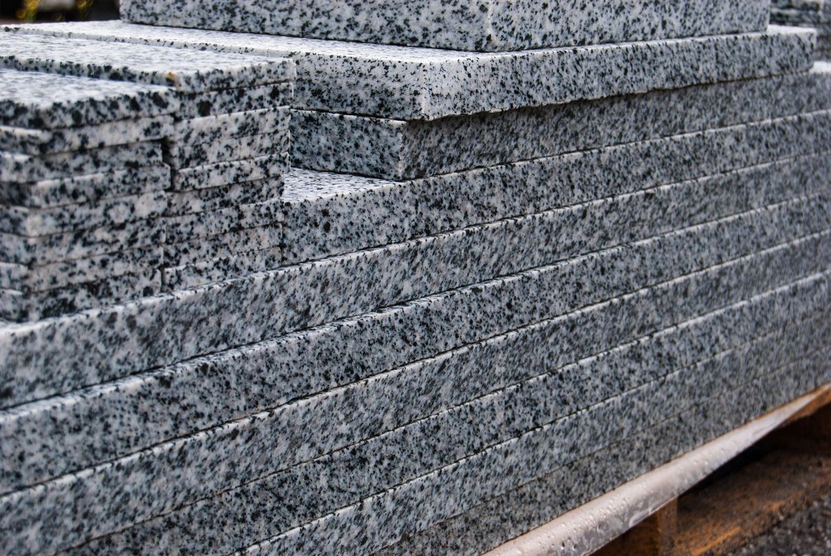 Lastre di granito grigio screziato impilate e appoggiate su un supporto di legno all'aperto.
