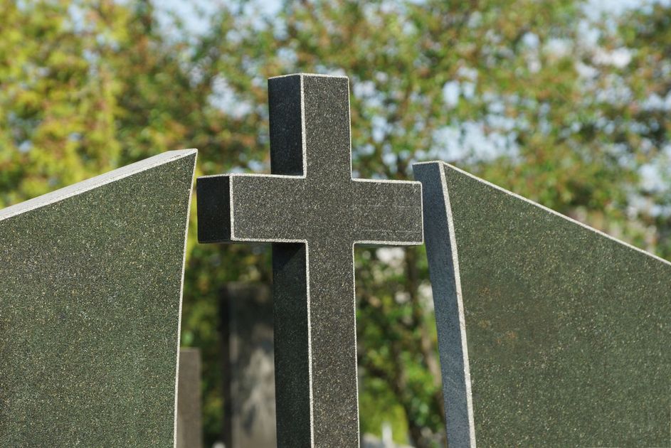Monumento a croce nera tra pannelli di pietra inclinati, all'aperto, con alberi sullo sfondo.
