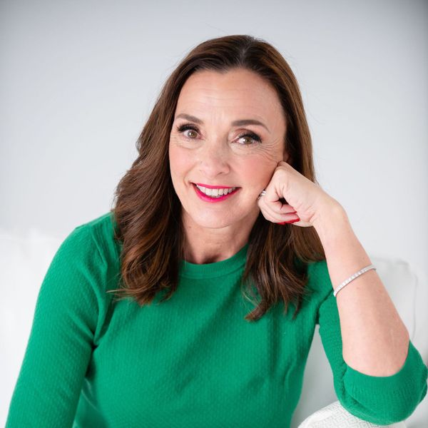 A woman in a green sweater is sitting on a couch and smiling.