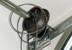 Garage door spring system with coiled spring, cable, and metal rod.