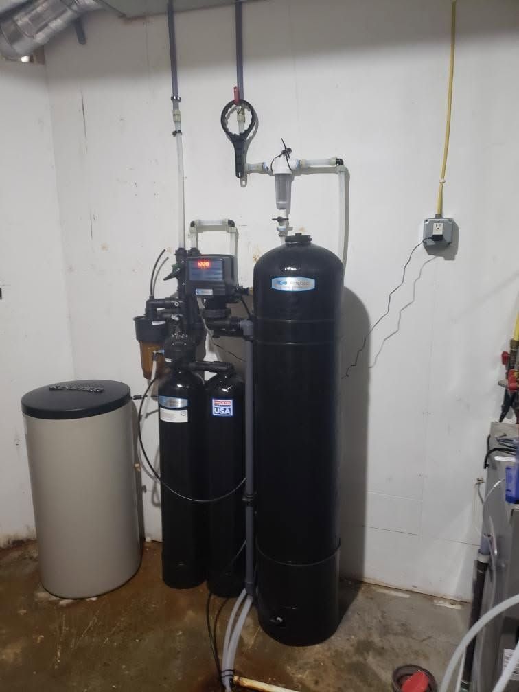 Water softener and filtration system with tall black tanks in a basement utility room