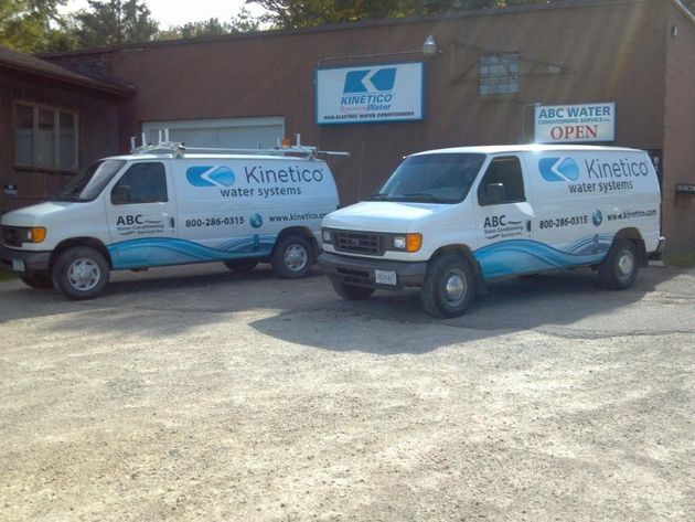 Two white Kinetic vans parked outside a building with a blue sign and open sign nearby