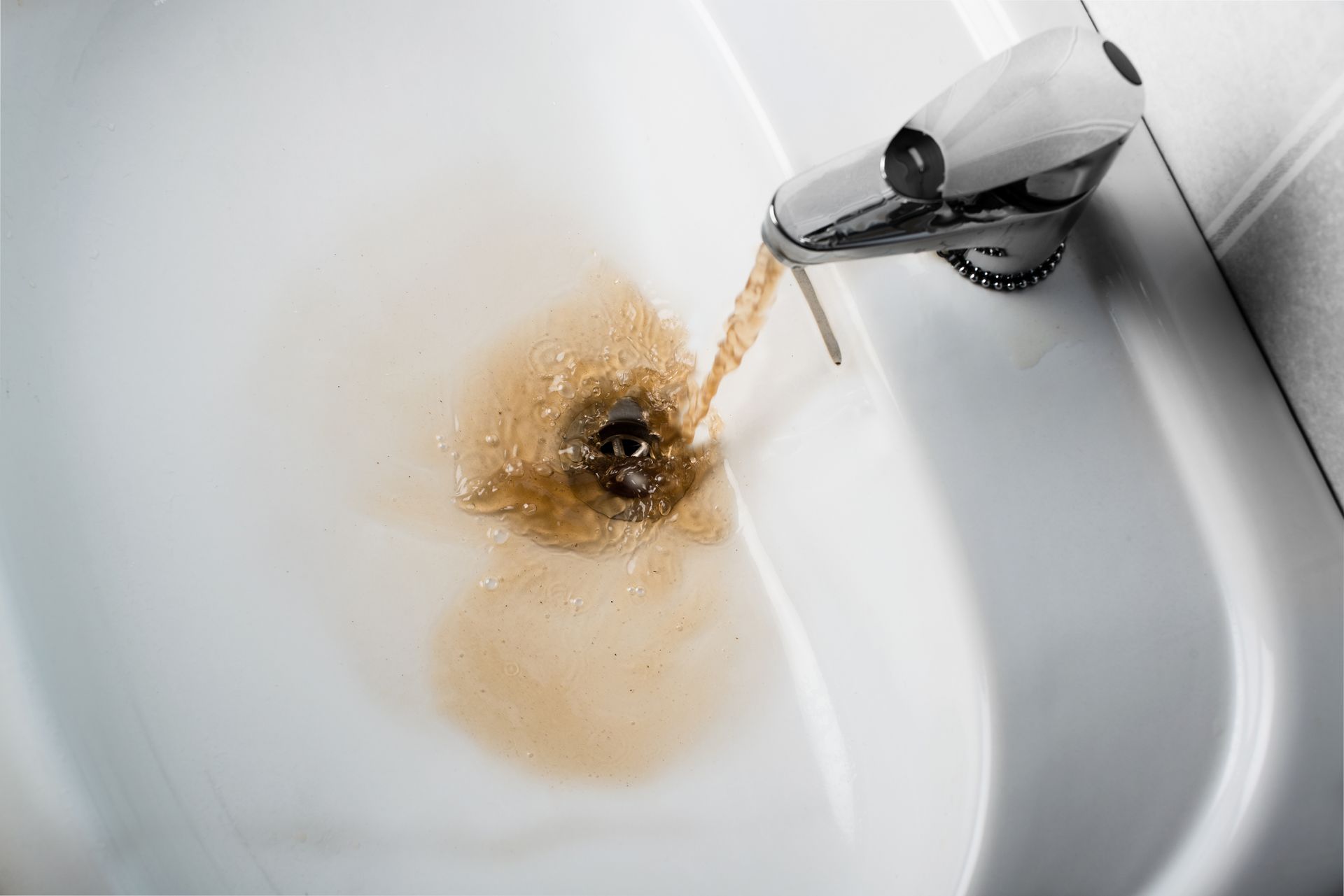 Brown water pouring from a faucet into a white sink, staining the drain area