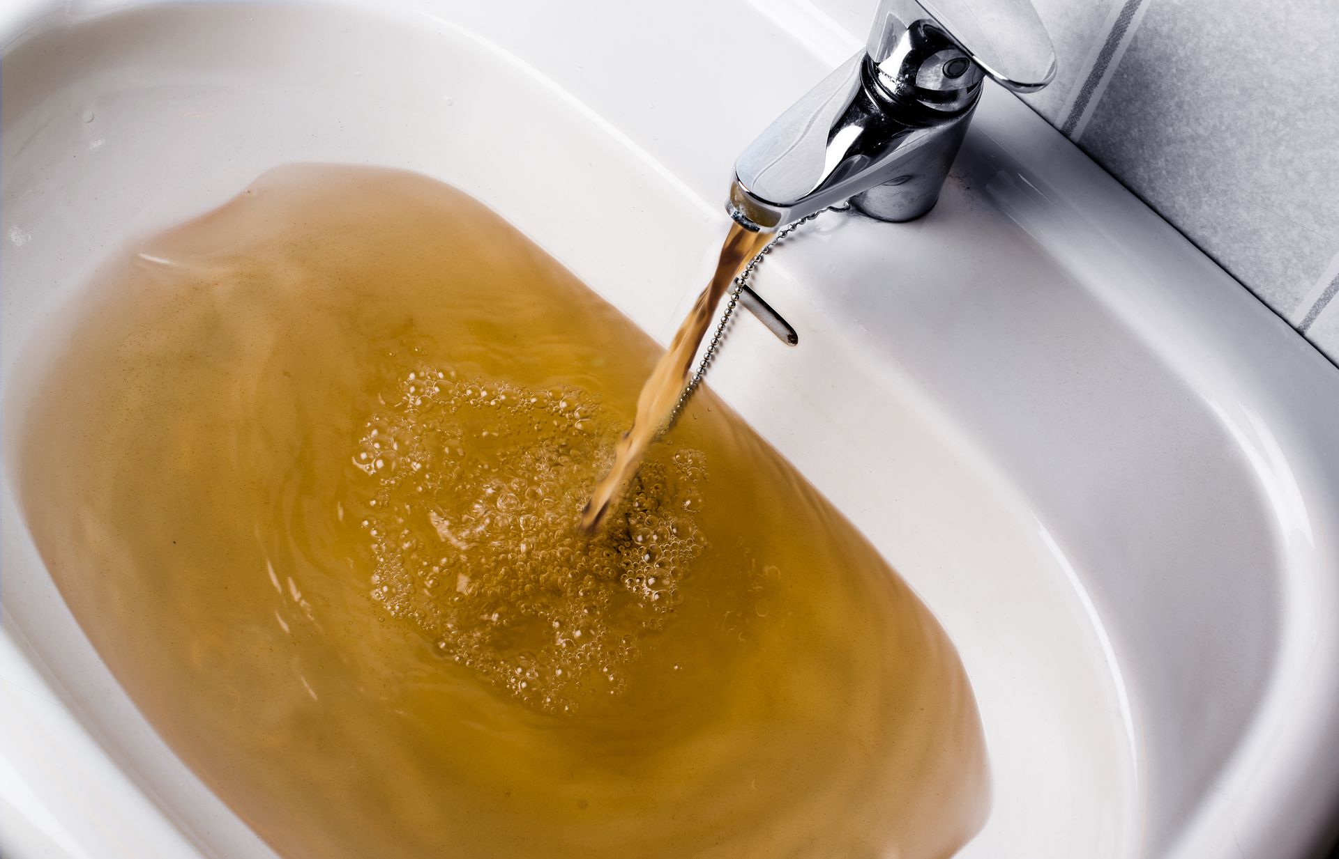 Brown water flowing from a faucet into a white sink