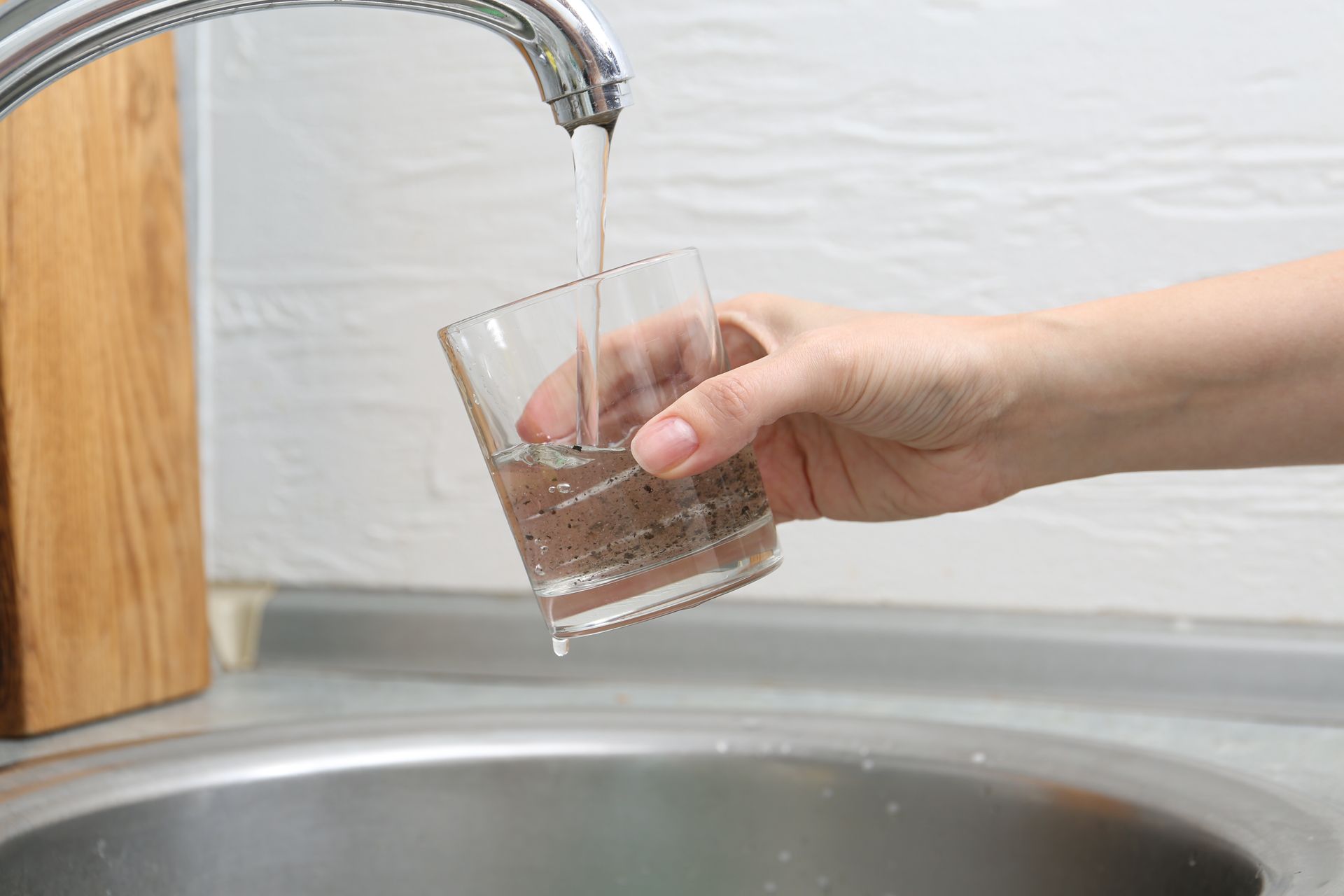 Hand pouring water from a faucet into a glass over a kitchen sink