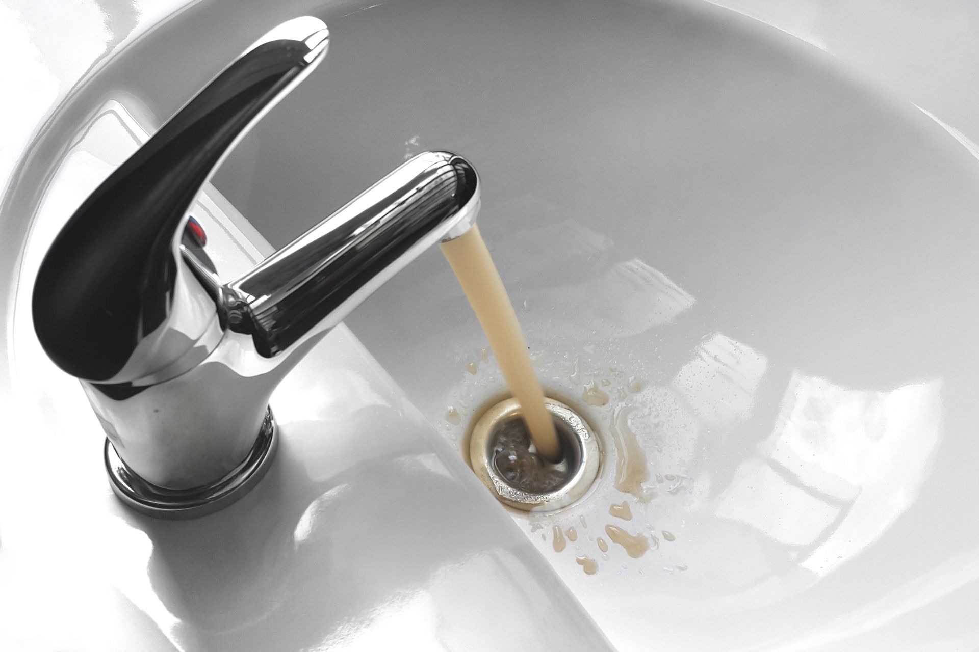 Water flowing from a chrome faucet into a white sink drain