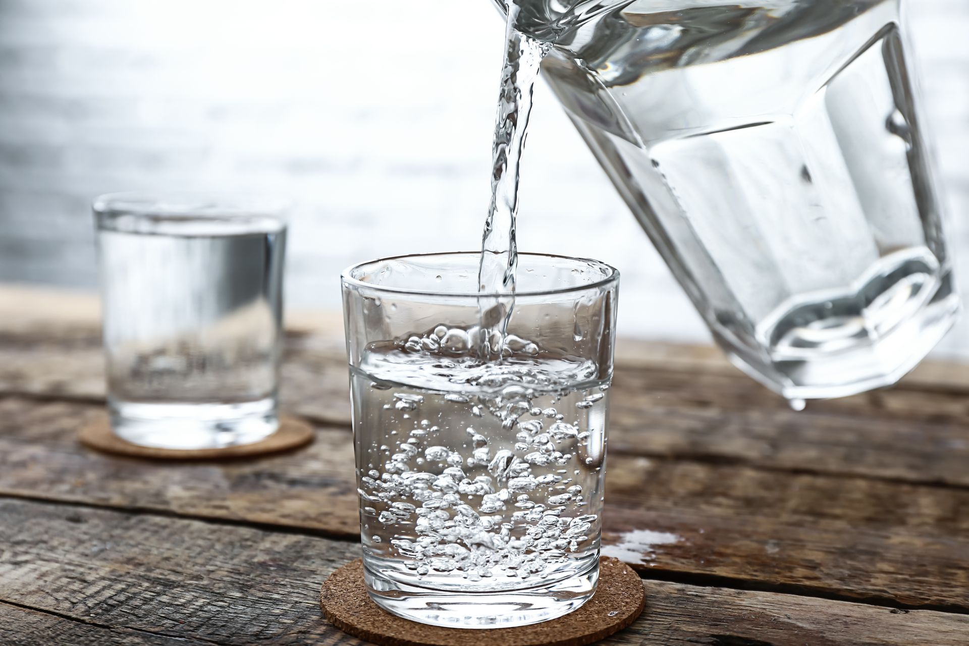 Water pouring into a clear glass on a rustic wooden table, with an empty glass beside it.