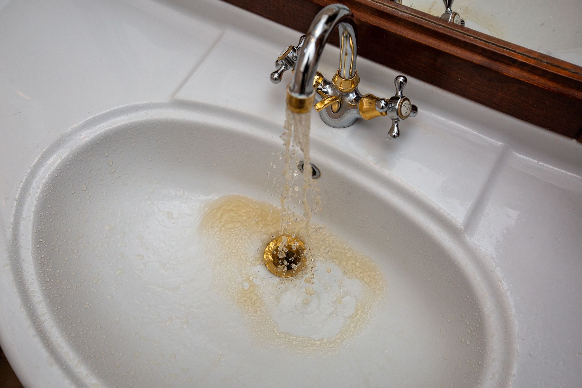Bathroom sink with running water and rusty discoloration around the drain
