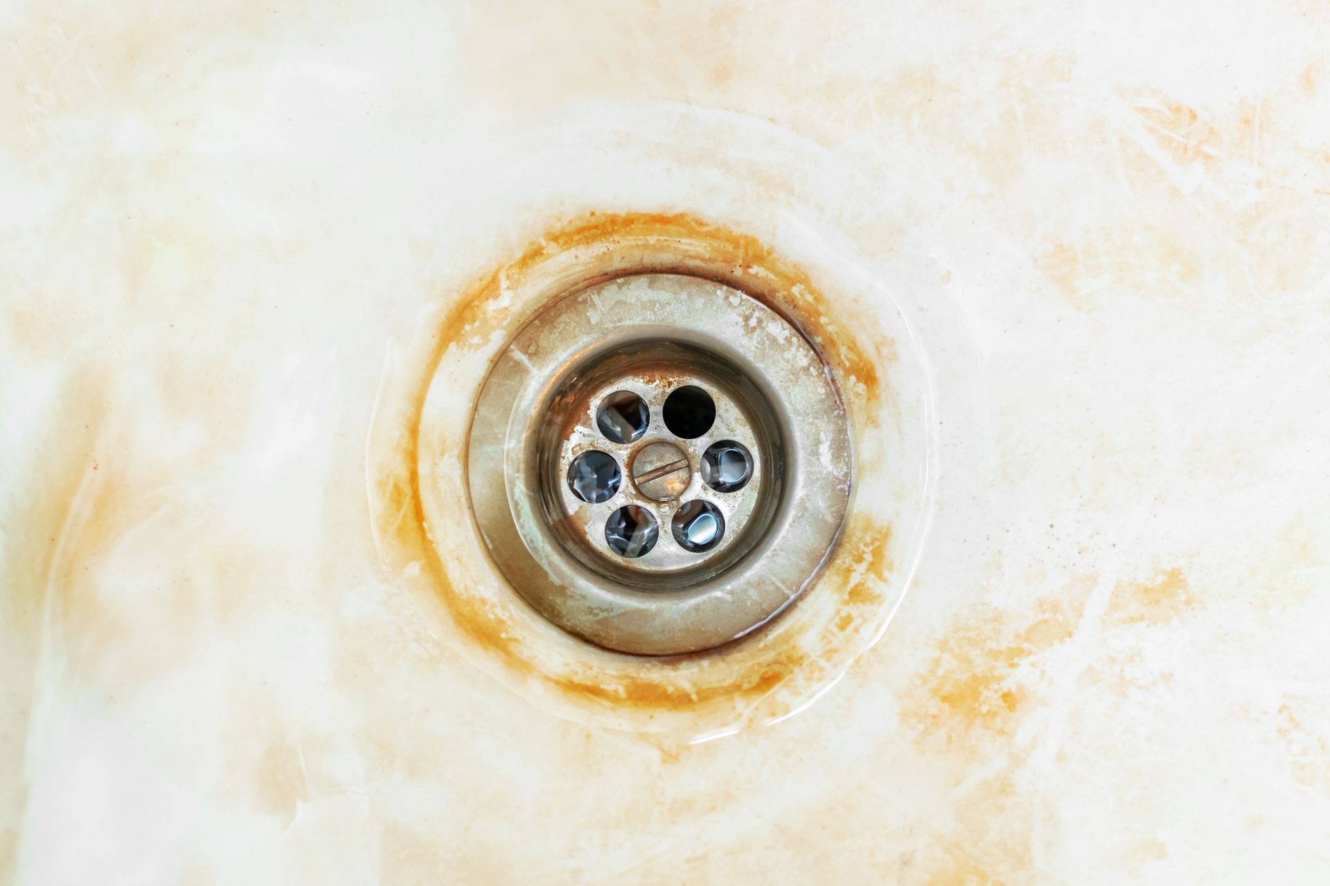 Close-up of a stained white sink drain with rust-colored rings and a metal strainer.