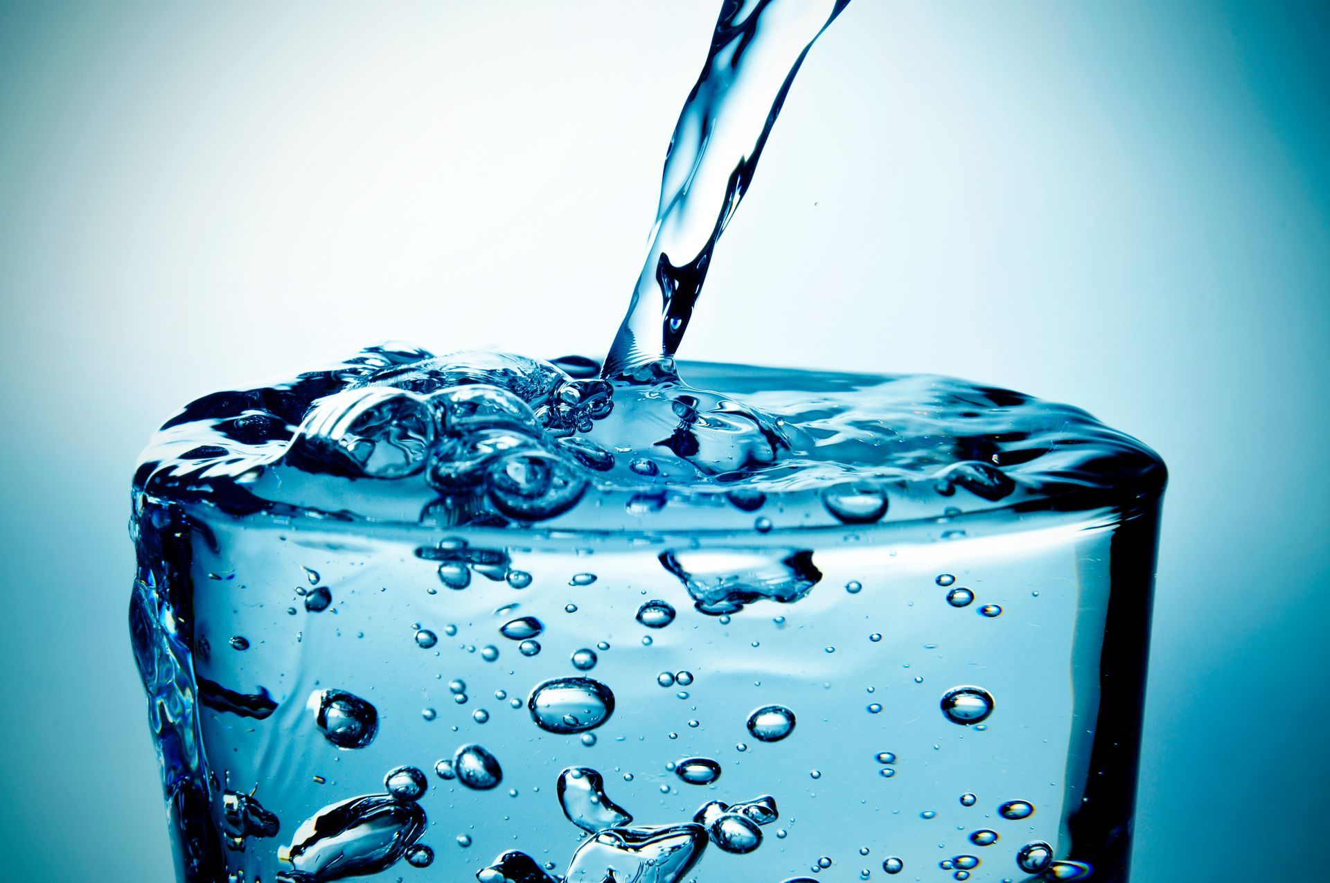 Water pouring into a clear glass, creating bubbles against a blue background
