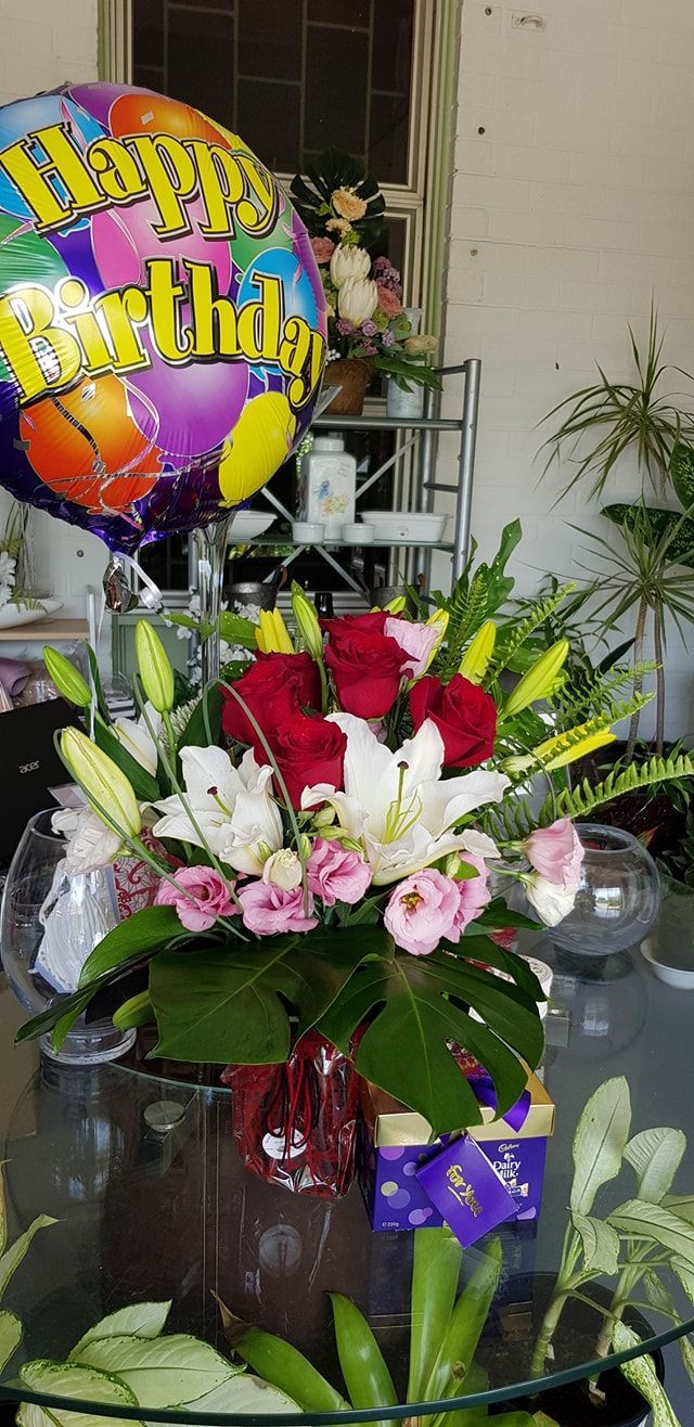 A Birthday Balloon is Sitting on a Table Next to a Vase of Flowers — Greenfield Blooms and Gifts In Wanguri, NT