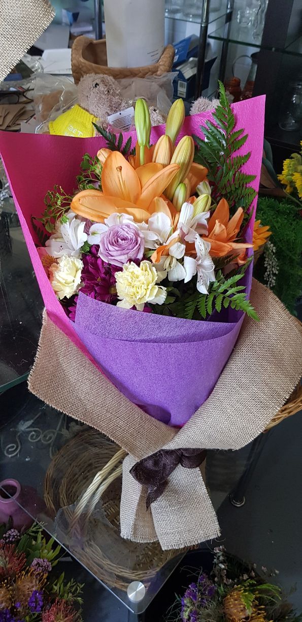 A Bouquet of Flowers Wrapped in Purple Paper is Sitting on a Table — Greenfield Blooms and Gifts In Wanguri, NT