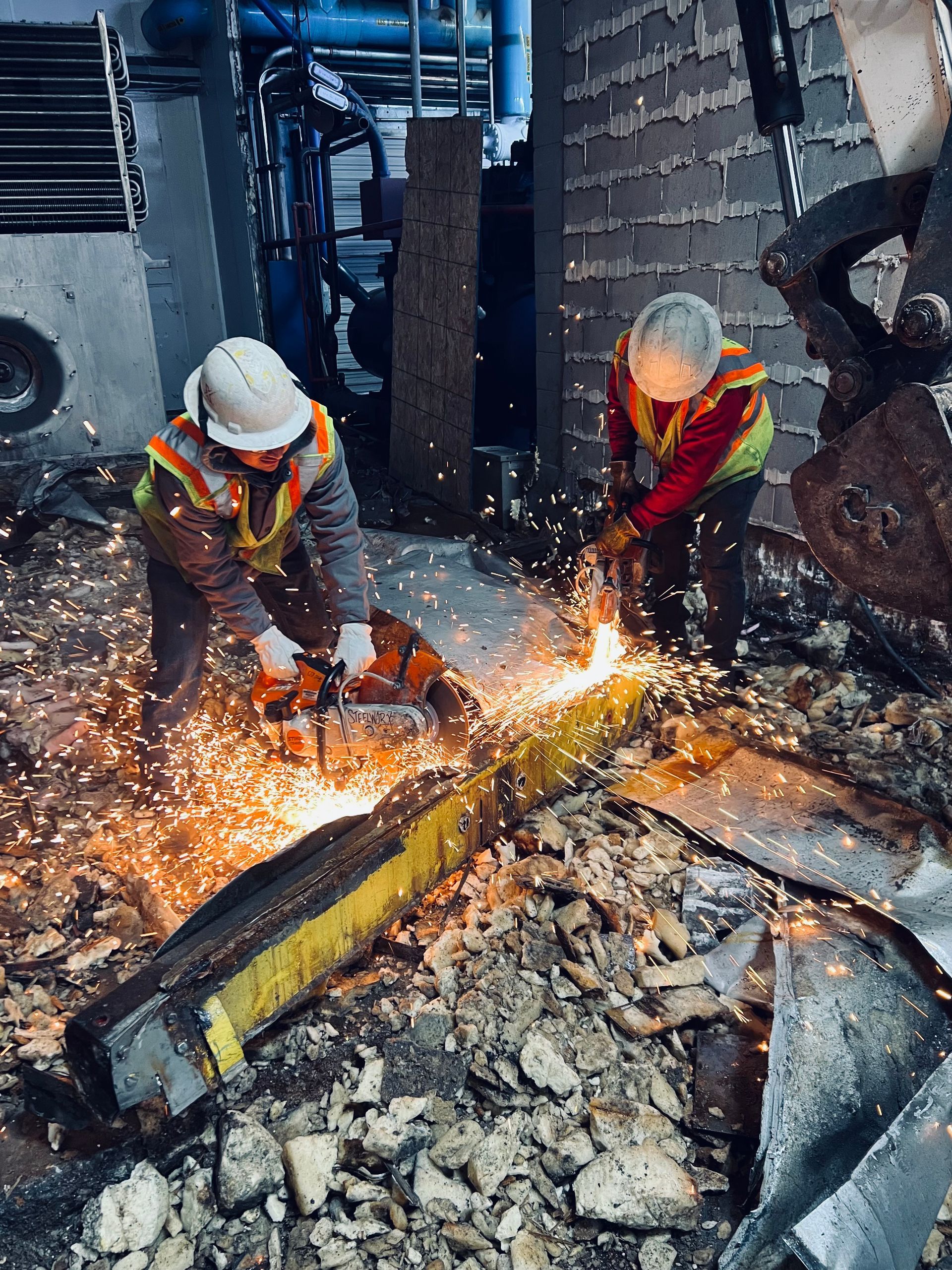 Two construction workers are cutting a piece of metal with a torch.