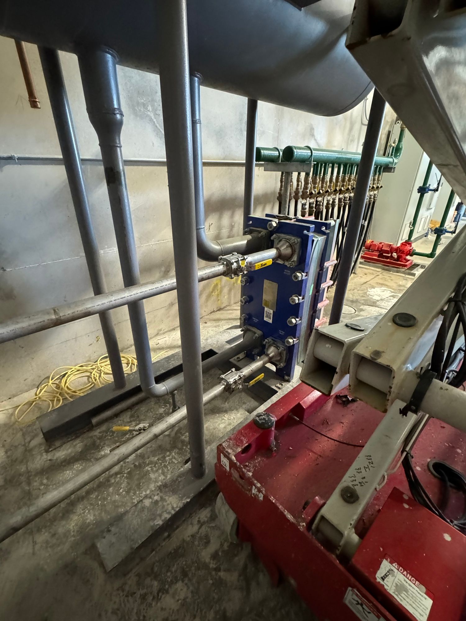 A red machine is sitting in a room with pipes.