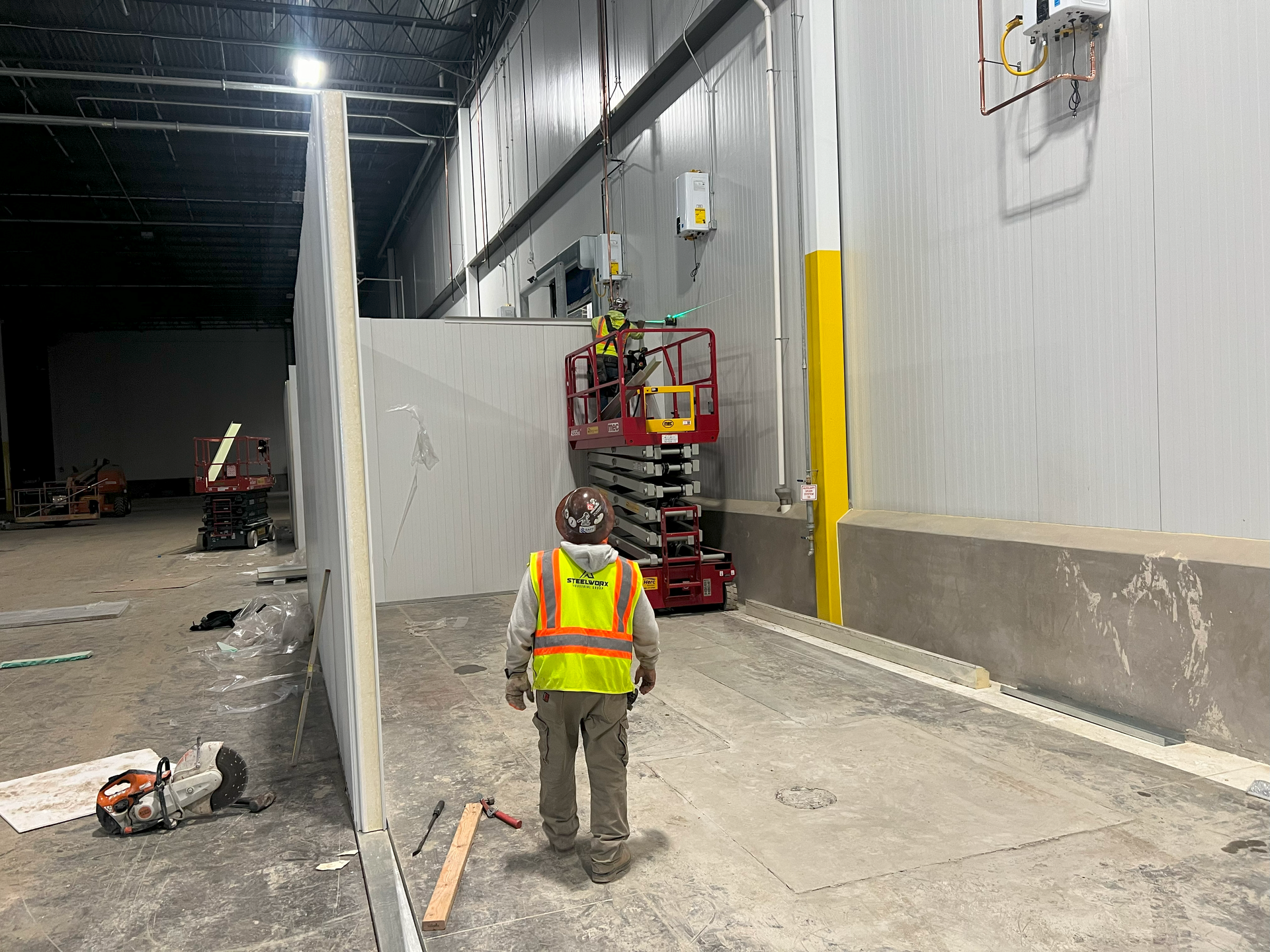 A man in a yellow vest is standing in a warehouse.