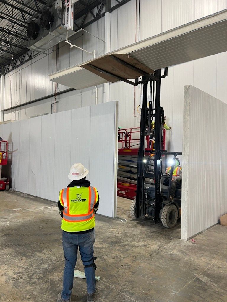 A man in a yellow vest is standing next to a forklift in a warehouse.