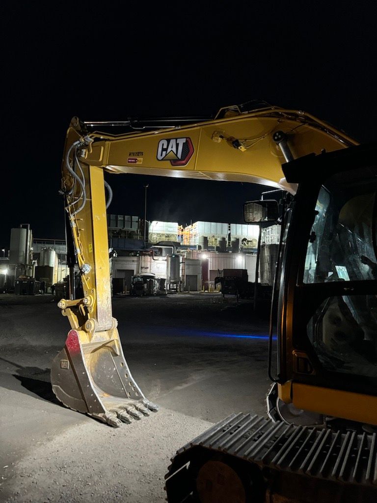A cat excavator is parked in a parking lot at night.