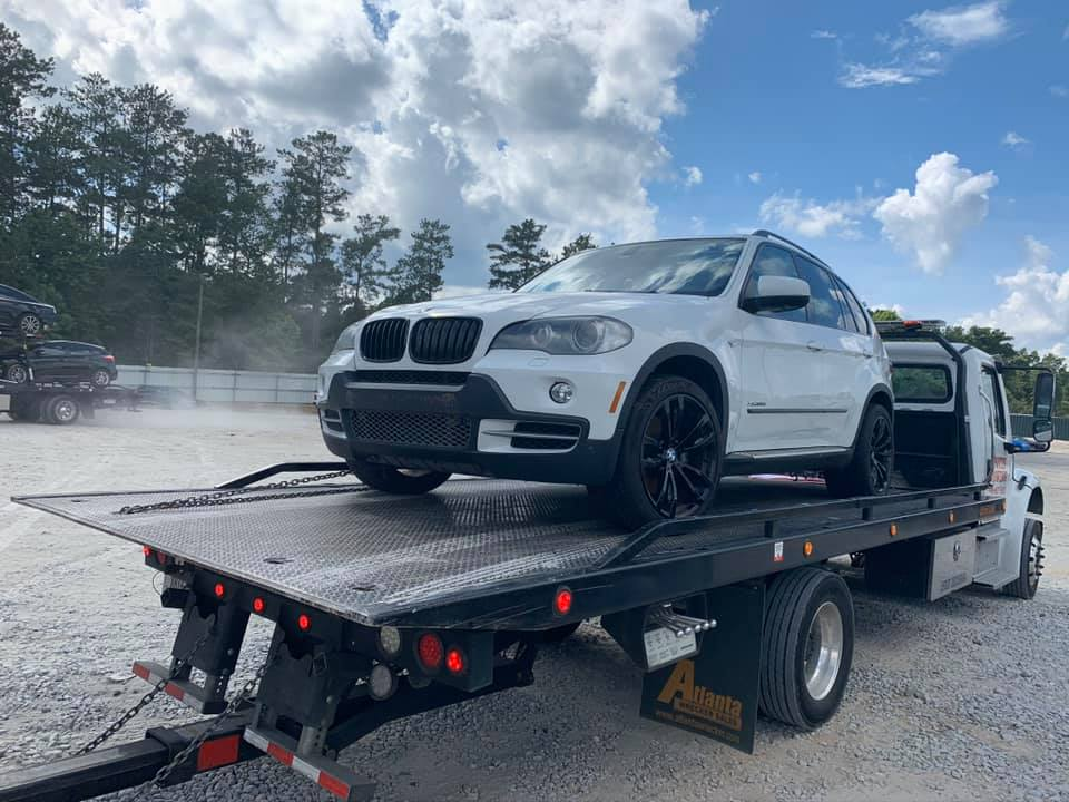 White BMW SUV on a flatbed tow truck outdoors under a cloudy sky