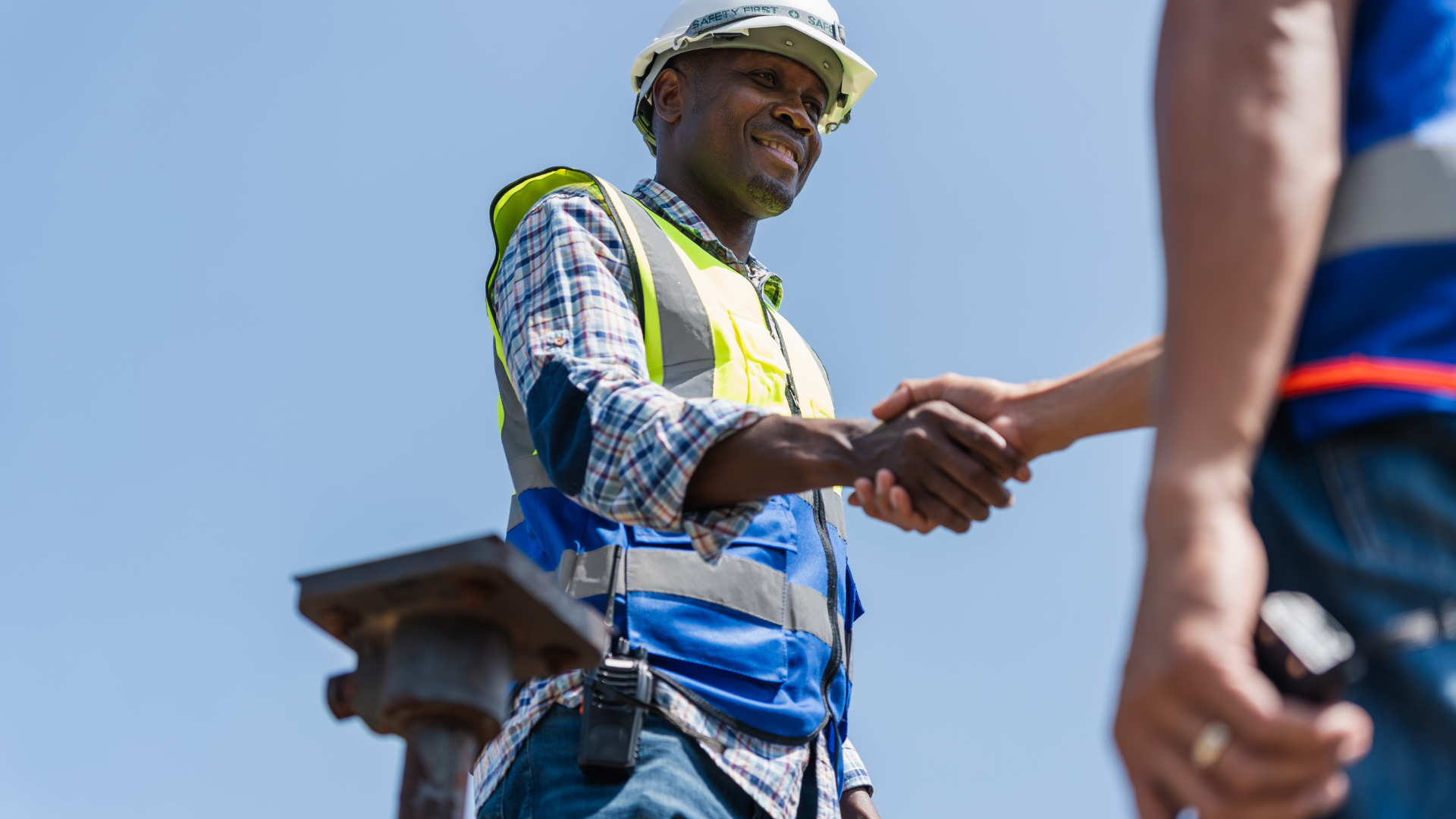Construction worker in safety vest and hard hat shaking hands outdoors.