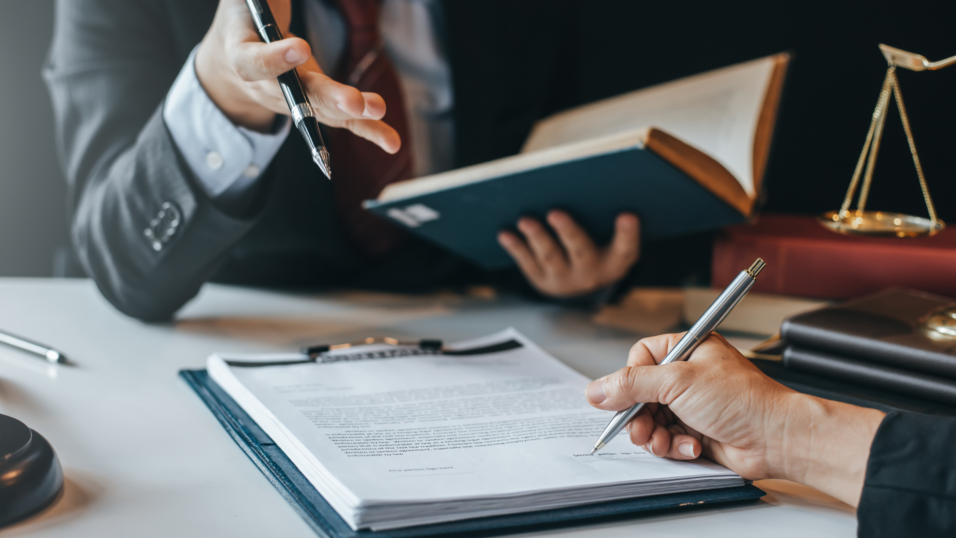Two people at a desk, one signing a document. Legal setting: scales of justice and law books.