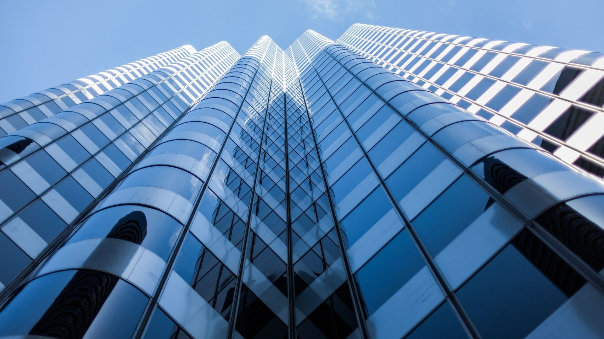 Low-angle view of a skyscraper with a mirrored glass facade against a blue sky.