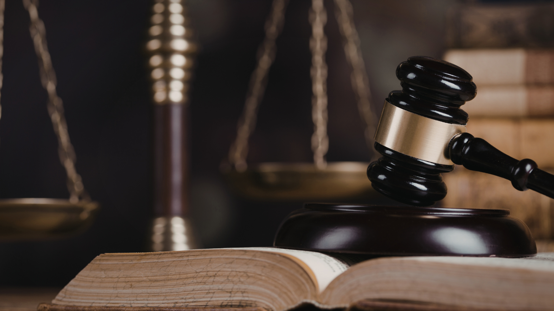 Gavel striking a wooden block on an open law book, with a balance scale in the background.