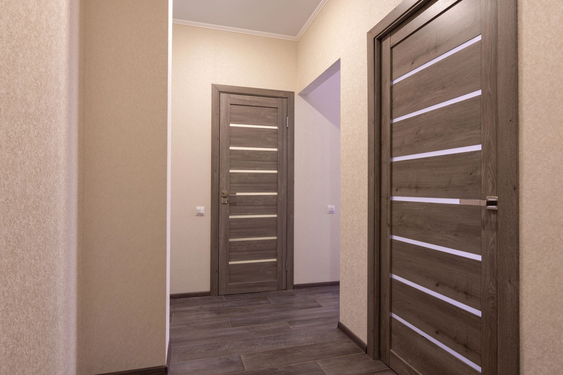 Corridoio con due porte in legno, pareti chiare e pavimento scuro.