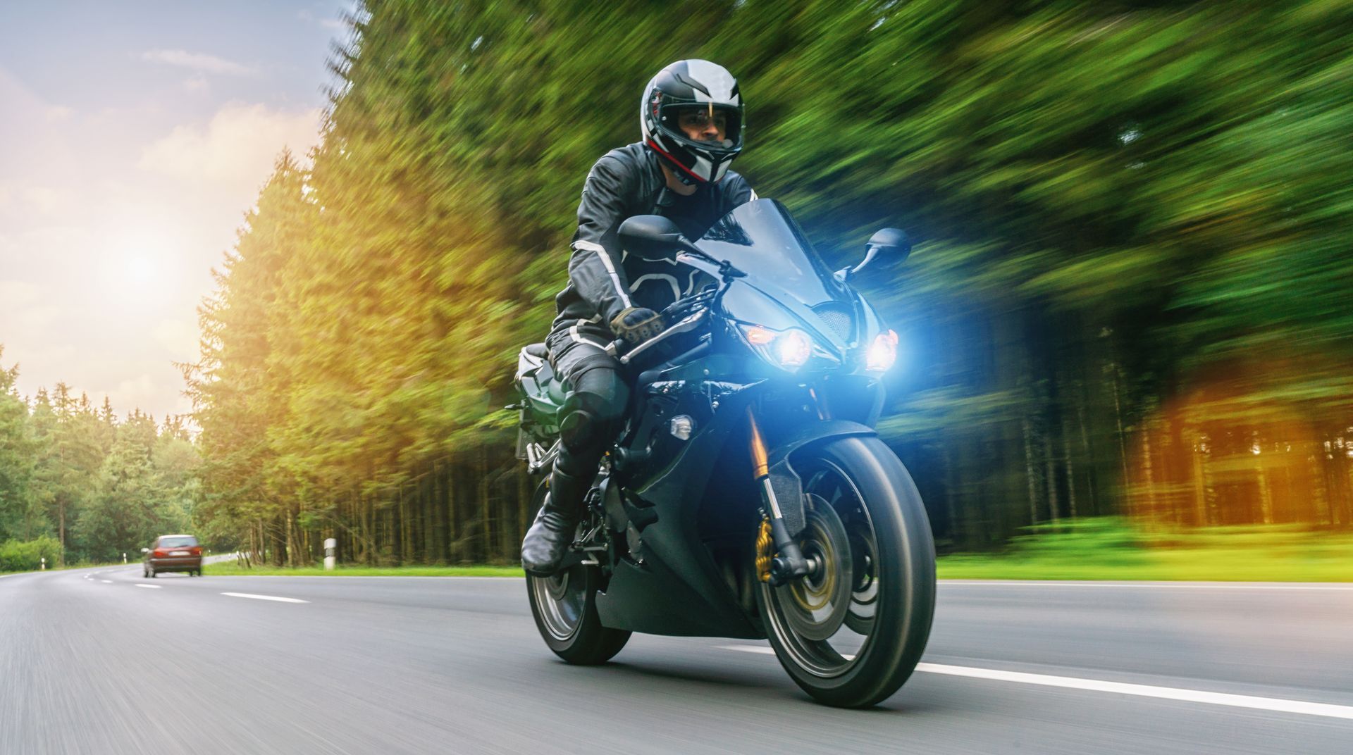 Motorcyclist rides on a forest road, leaning into a turn with bright blue headlight