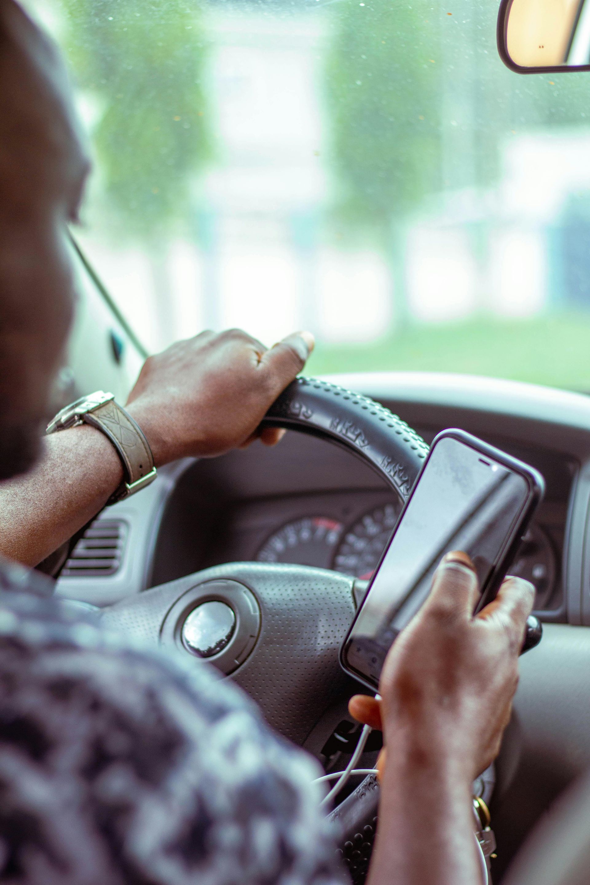 Person driving a car while holding a smartphone, with hands on the steering wheel.