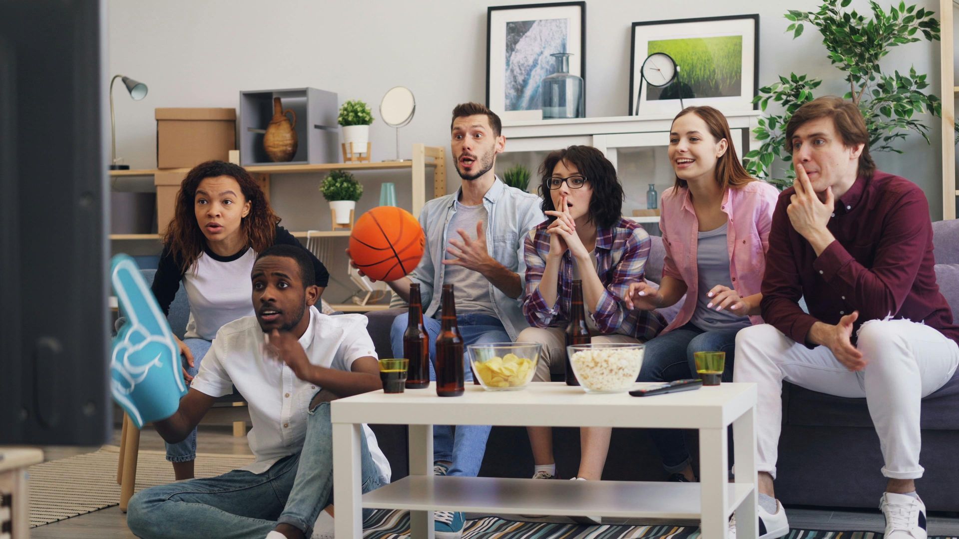 Friends watching a basketball game on TV in a cozy living room, cheering around a coffee table.