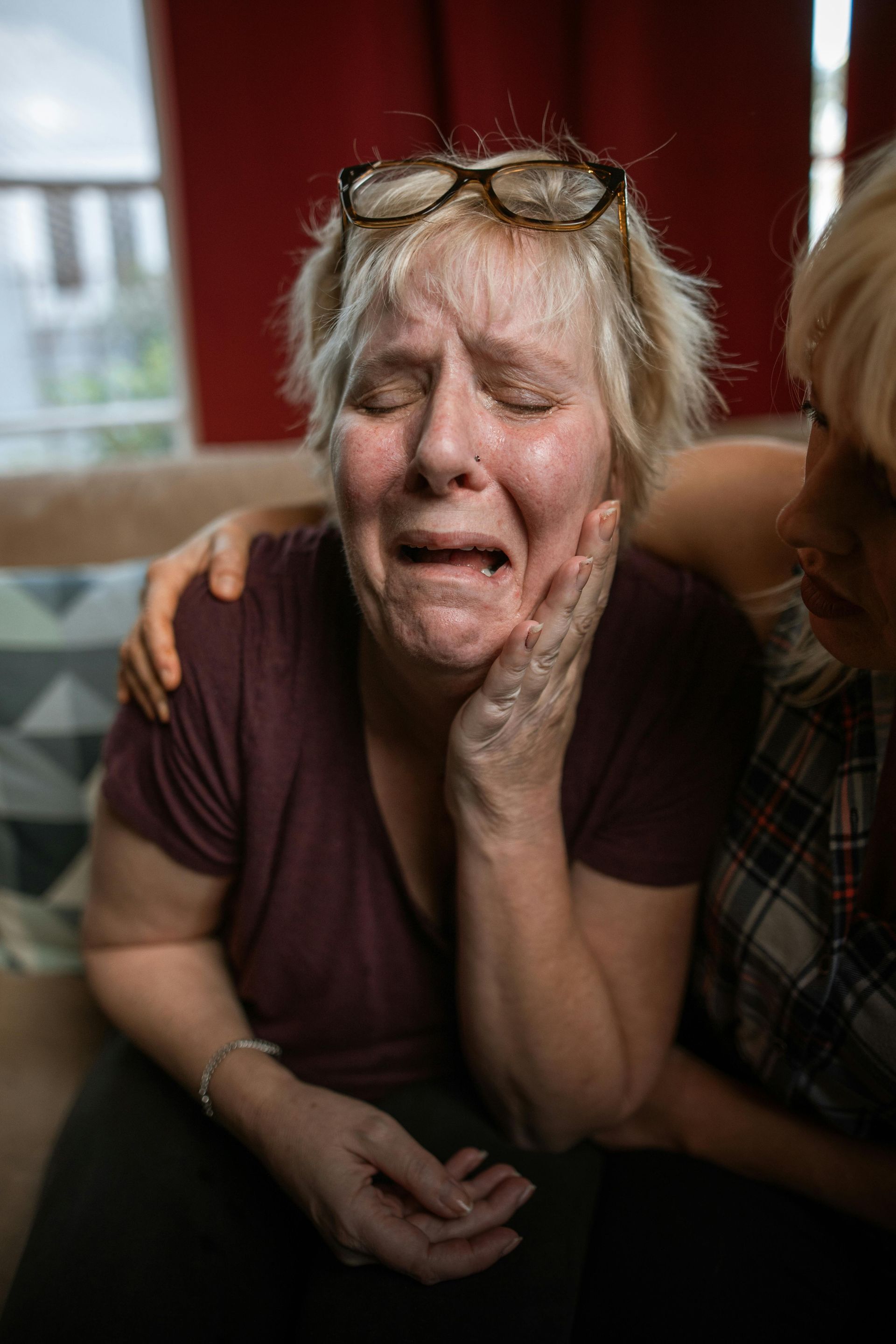 Distressed woman clutching her face as another person comforts her indoors