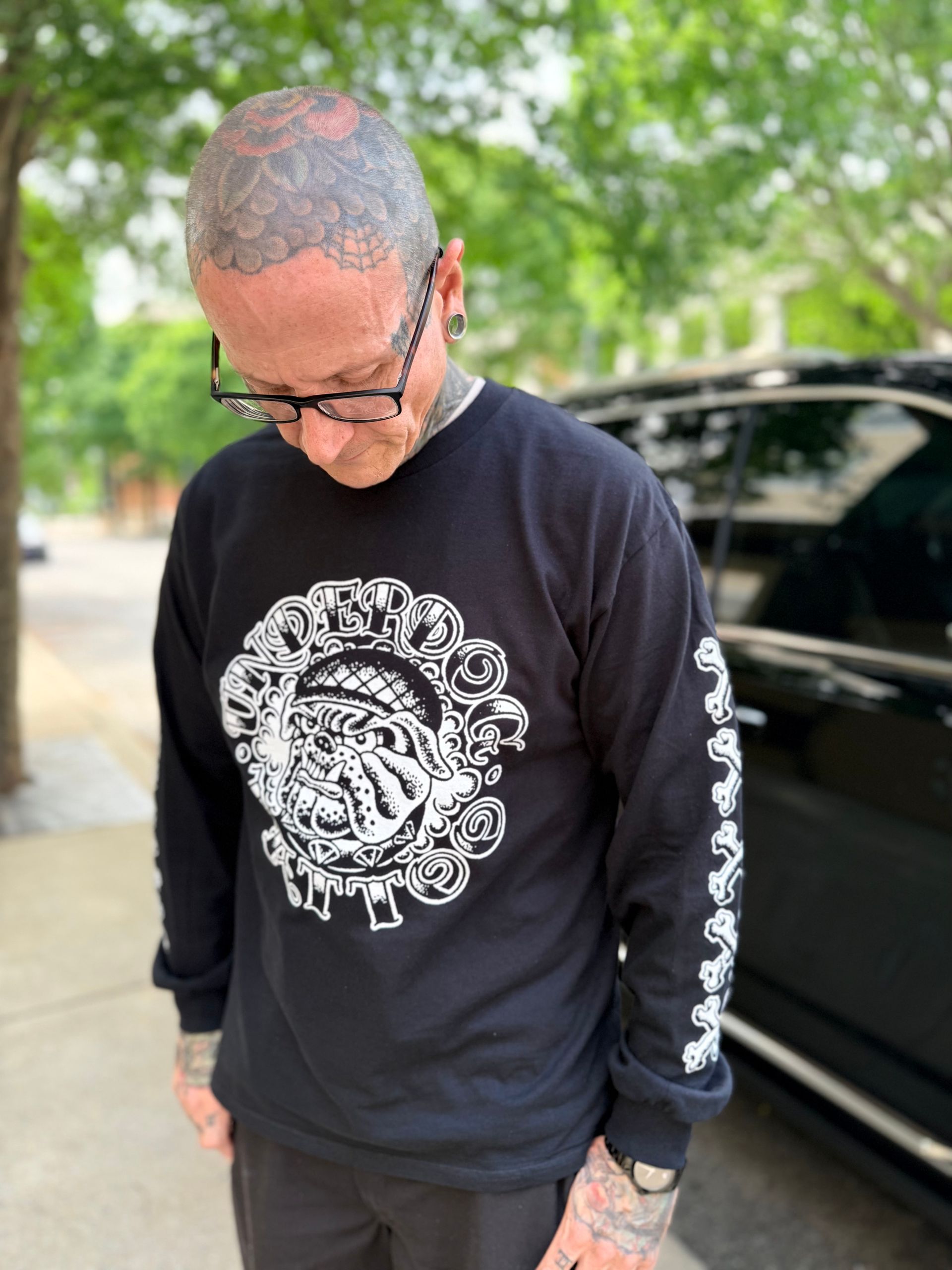 Man in black sweatshirt with white graphic and sleeve print looking down outdoors beside a parked car
