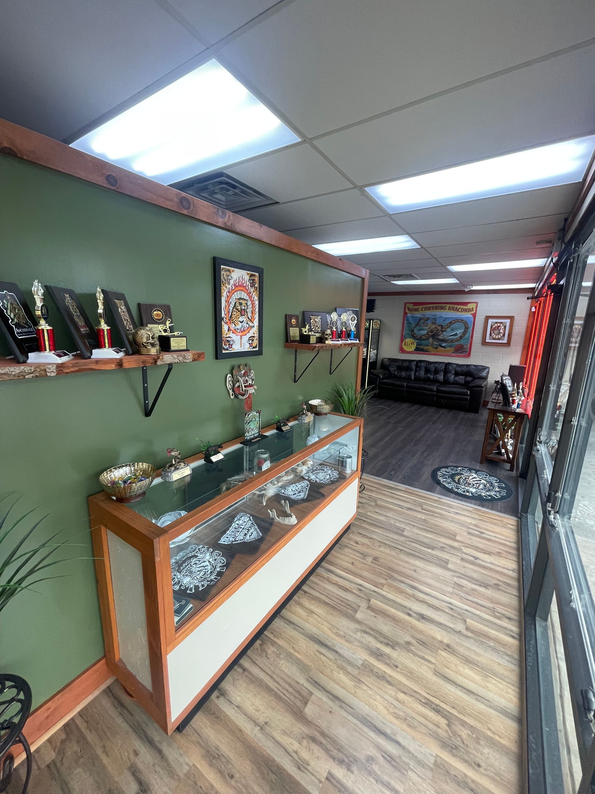 Small gallery or gift shop hallway with glass display cases, green walls, and overhead fluorescent lights.